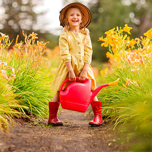 Hardlines Quality and Safety Child wearing yellow raincoat and red rainboots, holding a watering can